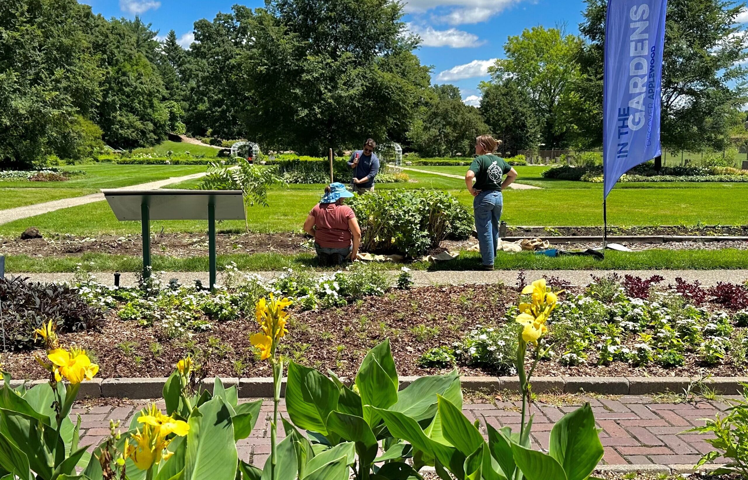 Three people work on a garden plot near a large blue feather banner that reads 