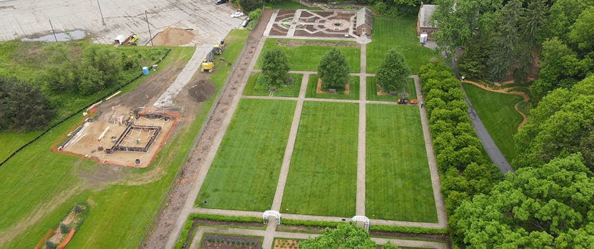 Aerial view of a landscaped garden within the Applewood Estate Master Plan featuring rectangular lawns, pathways, and trees. On the left side, construction work includes a partially built structure and visible equipment.