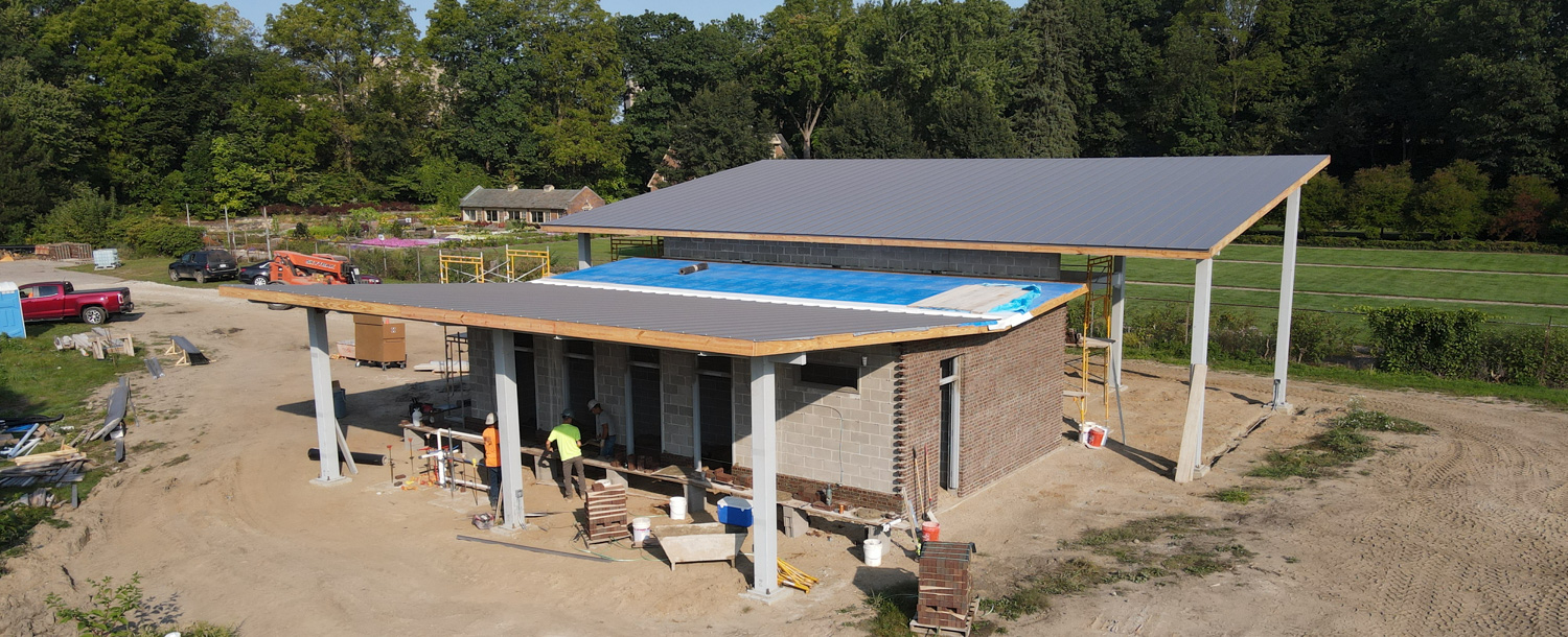 Construction site of a building with a partially completed roof, surrounded by equipment and workers. The area is open with trees and greenery in the background, all part of the ambitious Applewood Estate Master Plan.